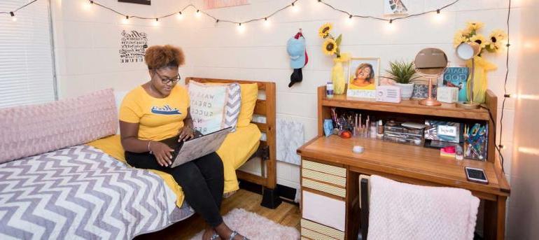 Girl sits in bed with laptop in her bedroom at boling apartments.