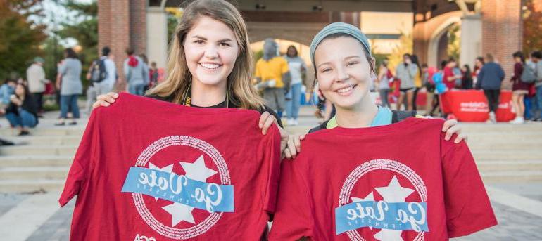two female students holding Mocs go vote shirts in hand 